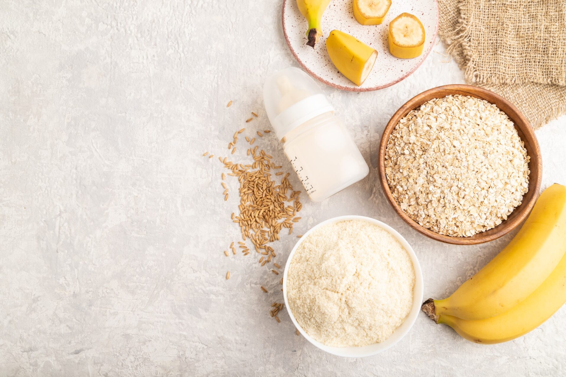 Powdered milk and oatmeal, banana baby food mix, on gray concrete, top view, copy space